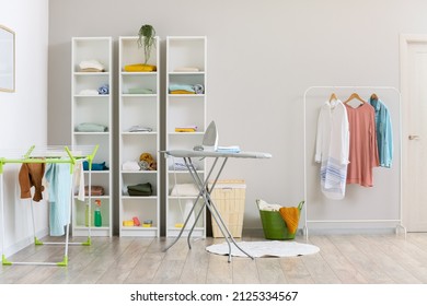 Interior of modern laundry room with ironing board and shelf units with different clothes - Shutterstock ID 2125334567