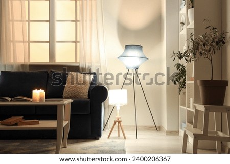 Interior of modern living room with black sofa, coffee table and glowing lamps at evening