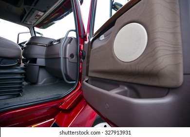 Interior Of Modern Luxury Red Semi Truck Made In Shades Of Brown Plastic. Through Open Door With Wood Paneling Truck Visible Part Of Seat With Shock Absorbers And The Dashboard Console With Air Vents.