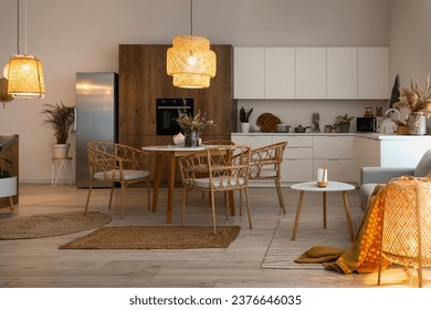 Interior of modern open plan kitchen with dining table, grey sofa and glowing lamps
