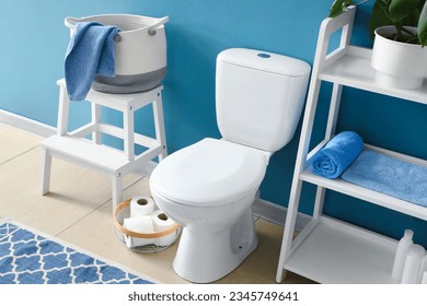 Interior of modern restroom with ceramic toilet bowl and shelving unit near blue wall