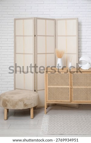 Interior of modern room with folding screen, pouf and chest of drawers