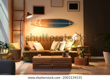 Interior of modern stylish room with surfboard and sofa in evening