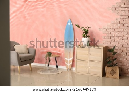 Interior of modern stylish room with surfboard and armchair near wall with print of clear water