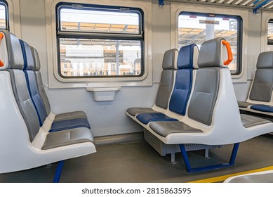 Interior of a modern train carriage featuring comfortable seating, staggered seat configuration, large windows allowing natural light, clean and contemporary design, platform view in background