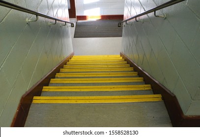 Interior Office School Staircase Stairway, Stone Steps With Yellow Edging Down Perspective Angle Falling Towards Floor With Bannister In Wood And Grey Brick Walls Wooden Railing & Skirting Boards