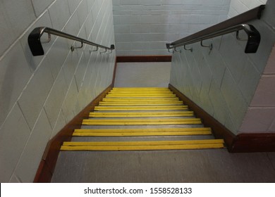 Interior Office School Staircase Stairway, Stone Steps With Yellow Edging Down Perspective Angle Falling Towards Floor With Bannister In Wood And Grey Brick Walls Wooden Railing & Skirting Boards