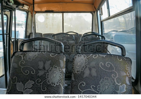 Interior of an old passenger bus. The\
seats are covered with grey upholstery, decorated with flowers. The\
inside of the vehicle is dirty and\
dusty.