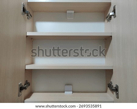 Interior of an Open and Completely Empty Light Wood Kitchen or Bathroom Cabinet, Showing Three Clean Shelves and Metal Door Hinges on a Neutral Background.