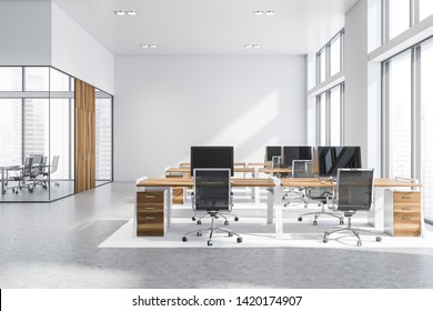 Interior of open space office with white walls, concrete floor, rows of wooden computer desks and meeting room in background. 3d rendering