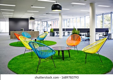 Interior photography of casual meeting areas in a corporate office with colourful Acapulco chairs, a coffee table, faux grass rug, planter boxes and an open plan office in the background