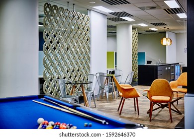 Interior Photography Of Commercial Fit Out Of Modern Office Break Out Area With Orange Chairs, Decorative Room Divider And Pool Table And Tables And Chairs With Kitchen In Background