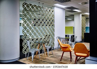 Interior Photography Of Commercial Fit Out Of Modern Office Break Out Area With Orange Chairs, Decorative Room Divider, Tables And Chairs With Office In Background