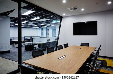 Interior photography of commercial fit out of modern board meeting room surrounded by glass walls & doors, wall mounted tv screen, open plan office in background