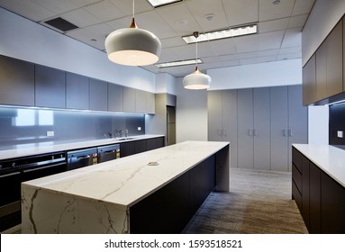 Interior Photography Of Commercial Fit Out Of Modern Office Break Out Area With Kitchen In Dark Tones, Marble Bench Tops, Pendant Lighting, Strip Lighting With Storage Cupboards In Background