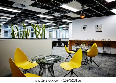 Interior Photography Of Commercial Fit Out Of Modern Office Break Out Area With Tall Lunch Table And Stools, Glass Topped Table And Yellow Plastic Chairs And Planter Boxes With Sansevieria