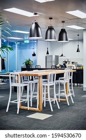 Interior Photography Of Commercial Fit Out Of Modern Office Break Out Area In Open Plan Office With Pendant Lighting, Lunch Table And Stools With Kitchen In Background