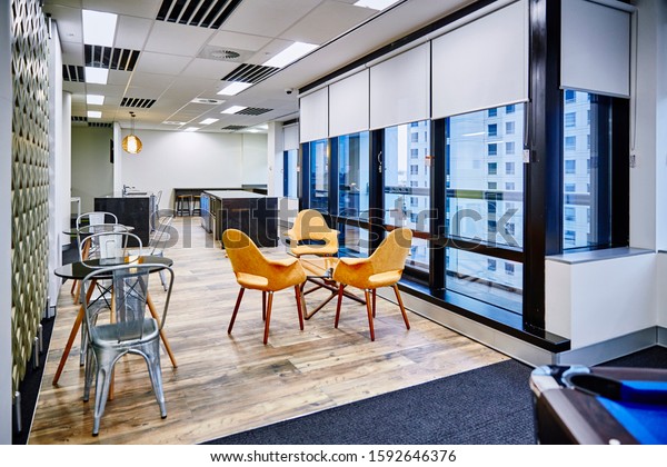 Interior photography of commercial fit out of\
modern office break out area with orange chairs, decorative room\
divider and pool table and tables and chairs with kitchen and city\
views in background