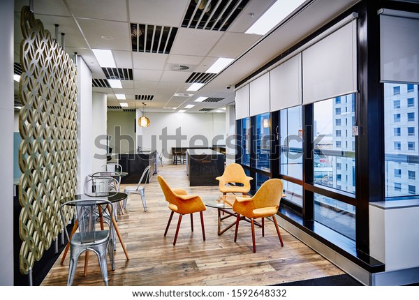 Interior photography of commercial fit\
out of modern office break out area with orange chairs and\
decorative room divider, kitchen and city view in\
background