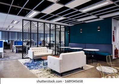 Interior Photography Of A Contemporary Design Corporate Office Break Out Area, A Lounge Area With Tables & Chairs With A Room Divider & Open Plan Office In The Background