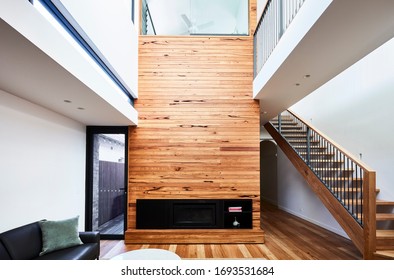 Interior Photography Of A Contemporary Lounge Room With A Timber Feature Wall And Fireplace, Polished Floor Boards And A Staircase To The Side