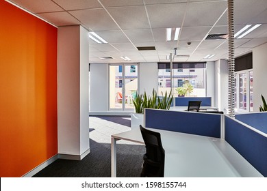 Interior Photography Of A Corporate Fit Out Open Plan Office Area With Desks, Filing Cabinets, Black Chairs, An Orange Feature Wall, Sansevieria Planter Boxes And A City View In The Background