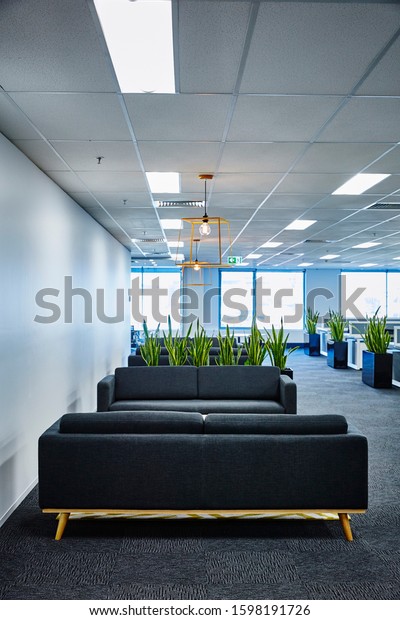 Interior\
photography of a corporate fit out open plan office with grey\
sofas, rug, coffee table, pendant lighting, yellow rug, planter\
boxes and open plan office in\
background