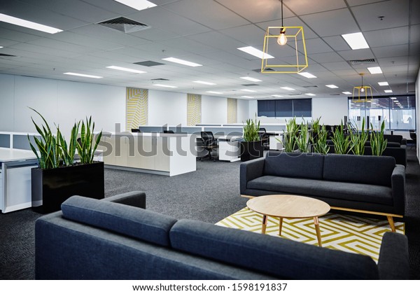 Interior\
photography of a corporate fit out open plan office with grey\
sofas, rug, coffee table, pendant lighting, planter boxes and open\
plan office and city views in the\
background