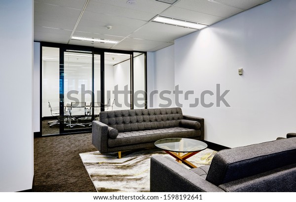 Interior photography of a corporate fit out\
open plan office with grey sofas, rug, coffee table, rug and\
meeting room in\
background