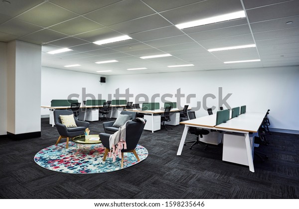 Interior photography of a\
corporate fit out open plan office with meeting area with grey\
sofas, colourful rug, coffee table and office cubicles in\
background