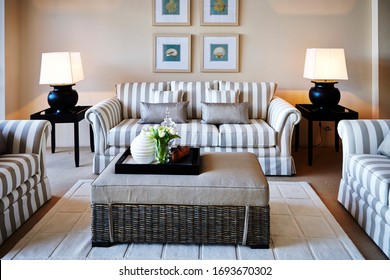 Interior Photography Detail Of A Classic Hamptons Style Lounge Room With Striped Sofas And Armchairs, Wicker Ottoman/coffee Table, Lamps, Side Tables, Framed Art On The Wall And A Rug