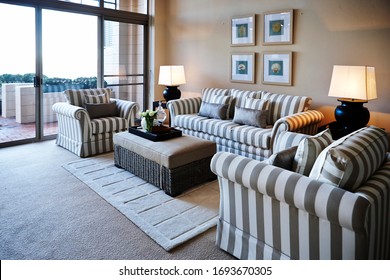 Interior Photography Detail Of A Classic Hamptons Style Lounge Room With Striped Sofas And Armchairs, Wicker Ottoman/coffee Table, Lamps, Side Tables, Framed Art On The Wall And A Rug