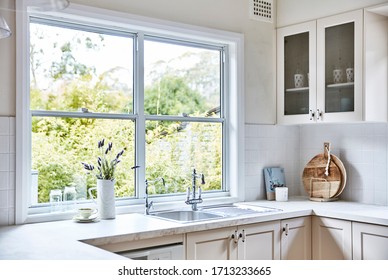 Interior Photography Of A Fresh White Hamptons Style Kitchen With A Marble Bench Top, Large Window Looking Out Onto A Back Garden