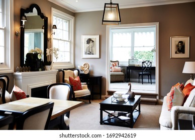 Interior Photography Of A Hamptons Style Formal Lounge Room With Wing Back Chairs, A Fireplace And A Sitting Room In The Background With Writing Desk And Arm Chairs