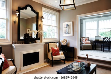 Interior Photography Of A Hamptons Style Formal Lounge Room With Wing Back Chairs, A Fireplace And A Sitting Room In The Background With Writing Desk And Arm Chairs