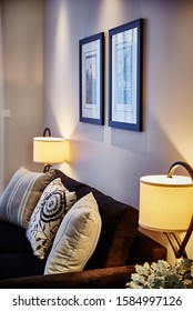 Interior Photography Of Hamptons Style Lounge Room With Dark Fabric Sofa, Framed Prints, Side Lamps And Scatter Cushions