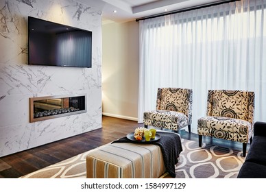 Interior Photography Of Hamptons Style Lounge Room With Printed Upholstered Arm Chairs, Ottoman Coffee Table, Rug, Marble Fire Place With Wall Mounted Tv