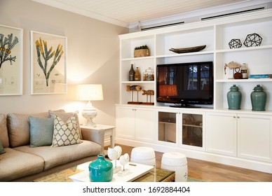 Interior Photography Of A Hamptons Style Lounge Room With A Beige Sofa, Coffee Table, Framed Botanical Art, A White Entertainment Unit With Tv & Decorative Objects