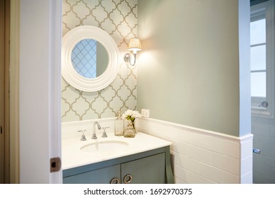 Interior Photography Of A Hampton's Style Powder Room Bathroom With Moroccan Print Wallpaper, A Round Mirror, Sconces And A Teal Painted Cabinet