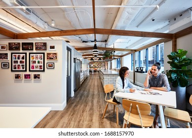 Interior Photography Of A Large Contemporary Design Corporate Office Break Out Area, Staff Holding A Meeting At A Lunch Table With A Kitchen In The Background