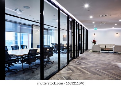 Interior Photography Of A Large Double Corporate Board Room With Concertina Doors, Beech Timber Meeting Tables, Parquetry Floor And A Reception Waiting Area On The Right With Grey Sofa And Arm Chairs