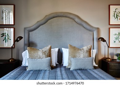 Interior Photography Of A Loft Bedroom In A Victorian Mansion, A Bed With An Upholstered Headboard, Cushions, Curtains And Framed Botanical Illustrations