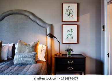 Interior Photography Of A Loft Bedroom In A Victorian Mansion, A Bed With An Upholstered Headboard, Cushions, Lamp And Framed Botanical Illustrations