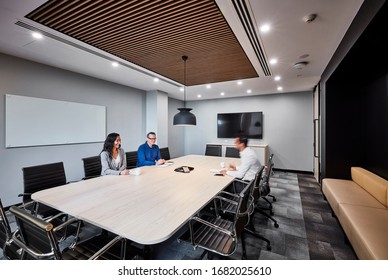 Interior Photography Of A Modern Corporate Board Room With A Large Beech Meeting Table, Black Leather Chairs, Timber Ceiling Detail, Pendant Lighting, Banquette Seating And Staff Holding A Meeting