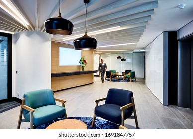 Interior Photography Of A Modern Corporate Office Reception Waiting Area With Blue Arm Chairs And Pendant Lighting With A Businessman Walking Through