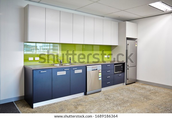 Interior photography of a modern\
corporate office break out area, an office kitchen with grey and\
white cabinetry, a green splash back and a polished concrete\
floor