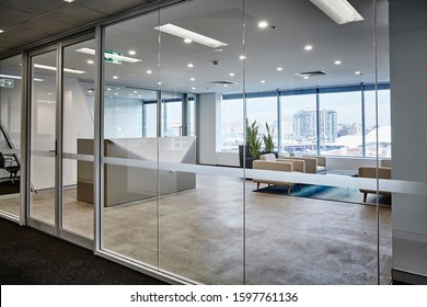 Interior Photography Of A Modern Corporate Reception Desk Area Viewed From Hallway With Concrete Flooring, Rug, Coffee Table, Grey Arm Chairs, Planter Boxes And City View In The Background