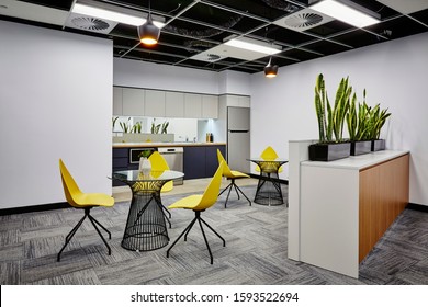 Interior Photography Of Modern Office Break Out Area With Kitchen, Pendant Lighting, Metal And Glass Topped Tables, Yellow Moulded Plastic Chairs, Planter Boxes With Sansevieria Plants