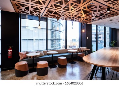 Interior Photography Of A Modern Office Breakout Area With A Timber Lunch Table, Decorative Laser Cut Wooden Ceiling, Polished Concrete Floors, Banquette Seating, Tables And Stools With A City View