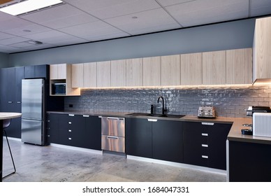 Interior Photography Of A Modern Office Breakout Area With Kitchen, Subway Tiles, Charcoal And Ash Cabinetry, Stainless Steel Appliances And Concrete Flooring